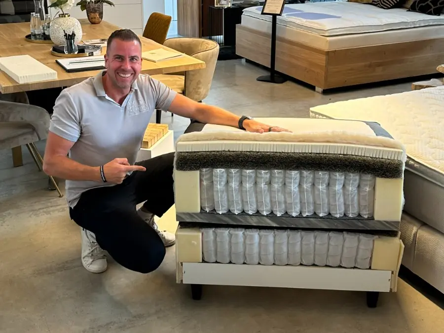 Ein Mitarbeiter zeigt im Showroom den offenen Aufbau eines Boxspringbetts mit zwei sichtbaren Federkern-Ebenen